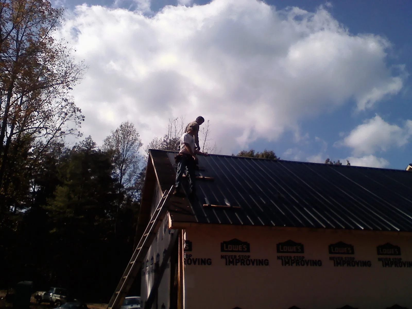 Roofer fastening dark metal panels high against a cloudy sky, from a Roof Inspection job in Yulan