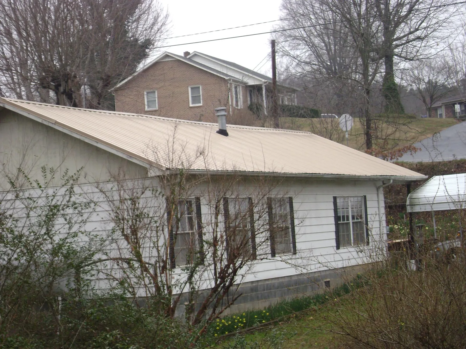Tan metal roof on a white sided house set into a hillside — Commercial Roofing by Roofing Brothers in Yulan