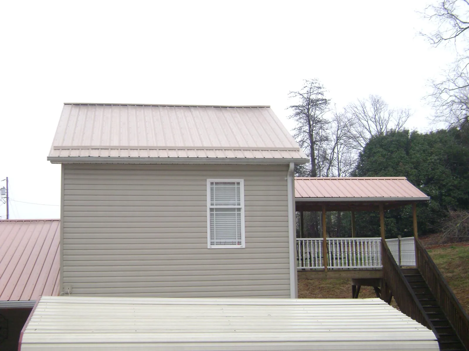 Tan metal roofs on a two story addition and attached porch, from a Roof Replacement job in Yulan